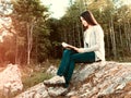 Young pretty girl reading a book sitting on a large rock in the forest Royalty Free Stock Photo