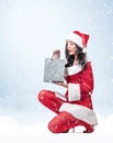 Young pretty girl in a red Santa outfit holds a gift bag in her hands, on a light blue background with snow Royalty Free Stock Photo