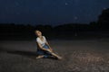 Young pretty girl sitting alone on the grass by the lake under the starry summer sky