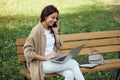 Young pretty woman sitting on bench at the park during summer day and using laptop. Royalty Free Stock Photo