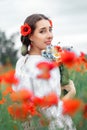 Young pretty girl Slavic or Ukrainian posing in folk dress on a flowering poppy field.