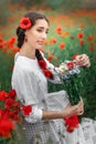 Young pretty girl Slavic or Ukrainian posing in folk dress on a flowering poppy field. Female holding a bouquet of Royalty Free Stock Photo