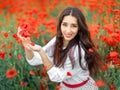 Young pretty girl Slavic or Ukrainian posing in folk dress on a flowering poppy field. Female holding poppy flowers with