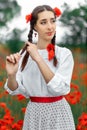 Young pretty girl Slavic or Ukrainian posing in folk dress on a flowering poppy field. Female weaving braid.