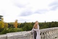 Young pretty girl standing near concrete railing with tree background.