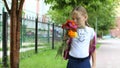 Young pretty girl standing near school with backpack and flowers sunny day. Back to school. Schoolgirl go to study Royalty Free Stock Photo
