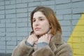 A young pretty girl stands near a brick wall in a beige fur coat without a hat and warms her hands in winter Royalty Free Stock Photo