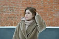 A young pretty girl stands near a brick wall in a beige fur coat without a hat in winter Royalty Free Stock Photo
