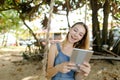 Young pretty girl using tablet and riding swing on sand, wearing jeans sundress. Royalty Free Stock Photo