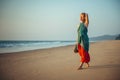 Young pretty girl walking along the seashore and admires the sunset. Blonde in bright clothes on sandy beach in the light of Royalty Free Stock Photo