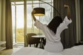 Young pretty girl wearing bathrobe and stretching in the morning in a hotel room facing the sunrise.