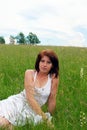 A young pretty girl in a white dress is sitting on a field on a hot summer day. Royalty Free Stock Photo