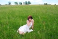 A young pretty girl in a white dress is sitting on a field on a hot summer day. Royalty Free Stock Photo