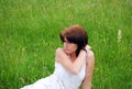 A young pretty girl in a white dress is sitting on a field on a hot summer day. Royalty Free Stock Photo