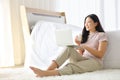 Young pretty girl working from home on her bed using computer laptop to access her work online while drinking a glass of milk Royalty Free Stock Photo