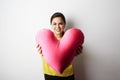 Young pretty girl in yellow tshirt holding big plush red heart over empty white background. Royalty Free Stock Photo