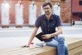 Young pretty guy in glasses working outside in park using modern tablet, notebook, mobile phone