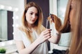 Young pretty hairdresser wearing casual clothes holding strand of long hair between fingers trimming the ends in beauty