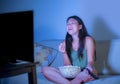 Young pretty and happy Asian Korean woman sitting at living room sofa couch watching television comedy show late night eating popc