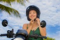 Young pretty happy and cute Asian Chinese woman adjusting motorcycle helmet riding on scooter motorbike isolated on a blue sky in Royalty Free Stock Photo