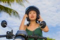 Young pretty happy and cute Asian Chinese woman adjusting motorcycle helmet riding on scooter motorbike isolated on a blue sky in Royalty Free Stock Photo