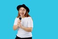 Young pretty happy woman in black hat singing a song with a microphone, isolated on blue background, studio portrait. Royalty Free Stock Photo