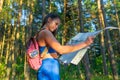 Young pretty hiker woman with backpack holding map in summer forest. Active lifestyle concept