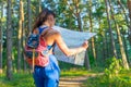 Young pretty hiker woman with backpack holding map in summer forest. Active lifestyle concept