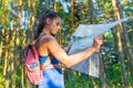 Young pretty hiker woman with backpack holding map in summer forest. Active lifestyle concept