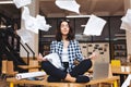 Young pretty joyful brunette woman meditating on table surround work stuff and flying papers. Cheerful mood, taking a Royalty Free Stock Photo