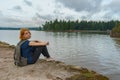 Young pretty lady with backpack sitting on bay shore in summer e Royalty Free Stock Photo