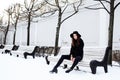 Young pretty modern hipster girl waiting on bench at winter snow park alone, lifestyle people concept Royalty Free Stock Photo