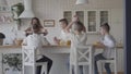 Young pretty mother bakes pies for her four teen sons in white shirts waiting for the food sitting at the table in the