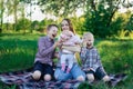 Young pretty mother with daughter and two sons on plaid in the park. Childrens laughter, happy childhood