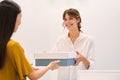 Young pretty positive fashion consultant happily giving shoes in box to client in store