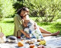 Young pretty pregnant brunette woman having fun with her daughter on picnic on green grass in park, lifestyle people