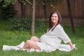 Young pregnant woman is sitting in the garden on the grass