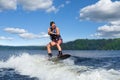 Young pretty slim brunette woman riding wakeboard on wave of motorboat in summer lake Royalty Free Stock Photo