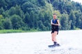 Young pretty slim brunette woman riding wakeboard on wave of motorboat in summer lake Royalty Free Stock Photo