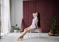 Young pretty slim brunette woman, wearing colorful light pink and grey pajamas with flowers pattern, sitting on black chair near