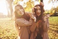 Young, pretty, and smiling brunette twin girls posing, having fun and playing with leaves, while wearing casual coat and Royalty Free Stock Photo