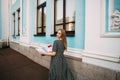 A young pretty smiling girl with blond hair, in a gray dress with a paper guide in her hands Royalty Free Stock Photo