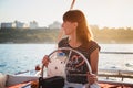 Young pretty smiling girl in striped shirt and white shorts driving luxury yacht in sea, hot summer day, sunset Royalty Free Stock Photo