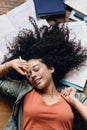 Young pretty smiling student girl with dark curly hair lying on floor with textbooks around and happily sleeping at home Royalty Free Stock Photo