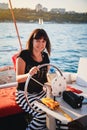 Young pretty smiling woman in black shirt and striped skirt driving luxury sailing boat in sea, sunset Royalty Free Stock Photo