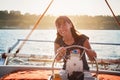 Young pretty smiling woman in striped shirt and white shorts driving luxury yacht in sea, sunset Royalty Free Stock Photo