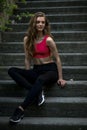 Young pretty sportive girl is sitting on the steps on the late summer evening looking down smiling