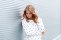 Young pretty stylish woman with blond hair in a stylish white sweater is resting near the modern metal wall in the city. Royalty Free Stock Photo