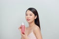 Young pretty stylish woman over white wall background holding bottle with cosmetics water