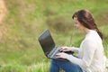 Young pretty successful smart business woman or student in light casual clothes sitting on grass using laptop in field Royalty Free Stock Photo